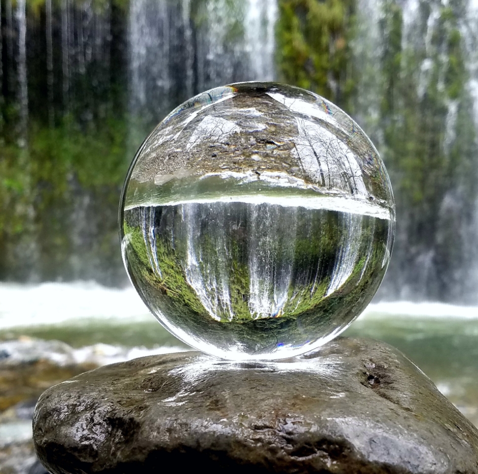 Glaskugel auf einem Stein liegend vor einem Wasserfall
